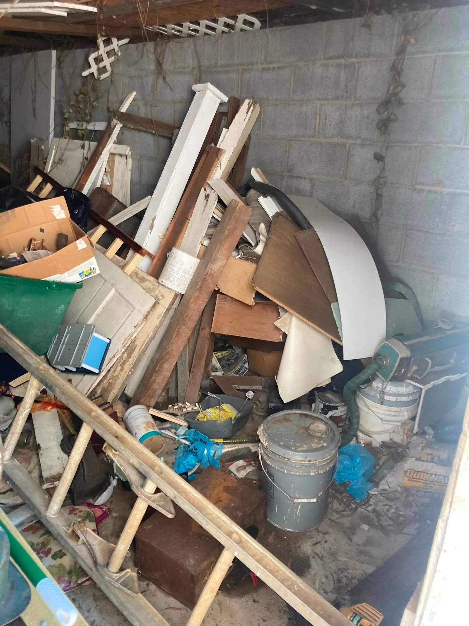 The interior of a block-wall storage shed packed with an old door, trim boards, paint cans, and buckets.