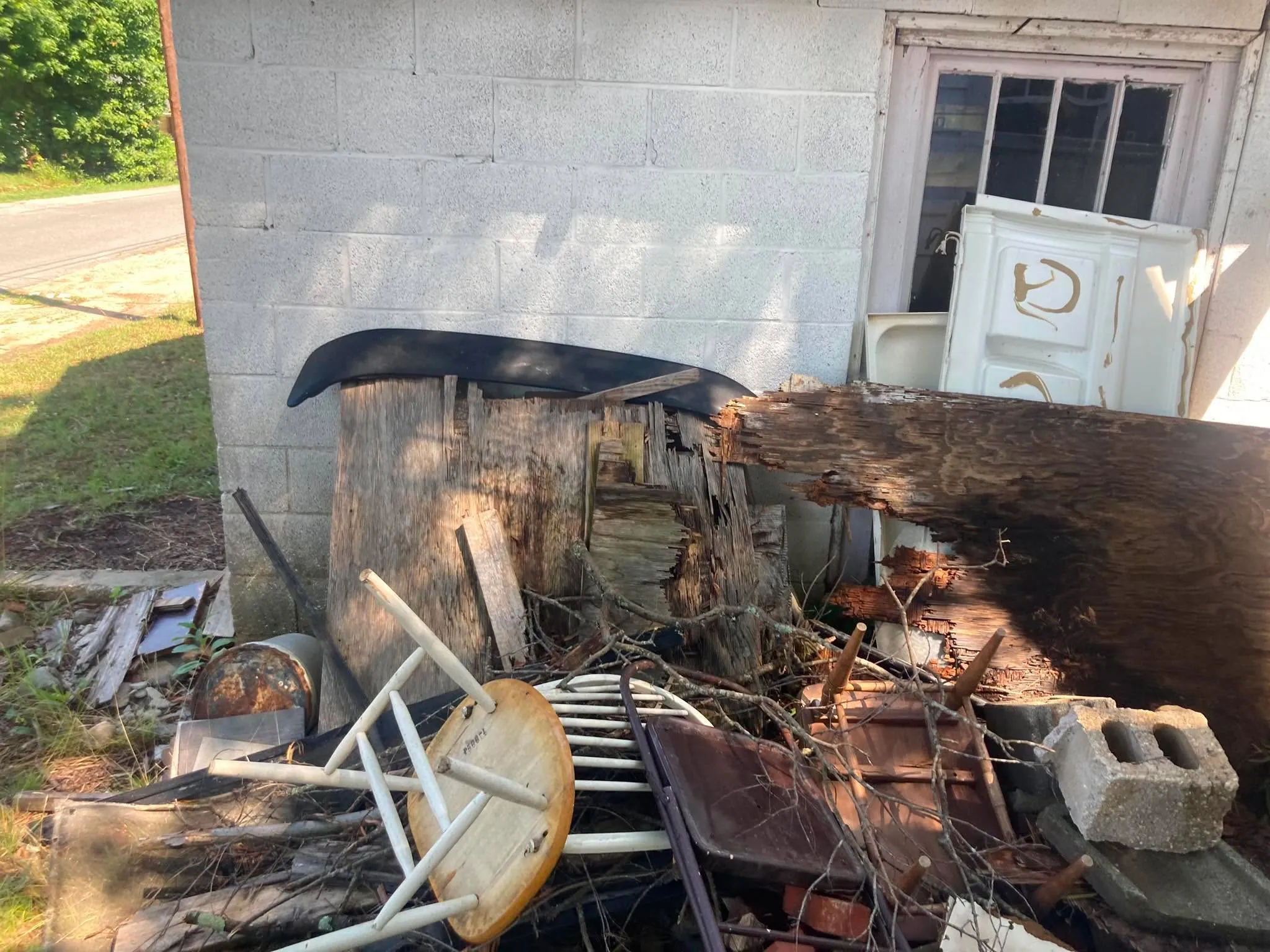 A pile of old chairs and broken wood stacked against the outside wall of a concrete block building.