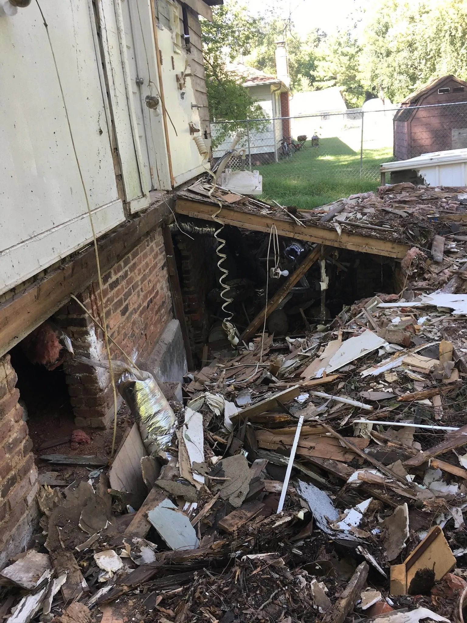 A pile of demolition debris beside a brick foundation wall with an open vent.