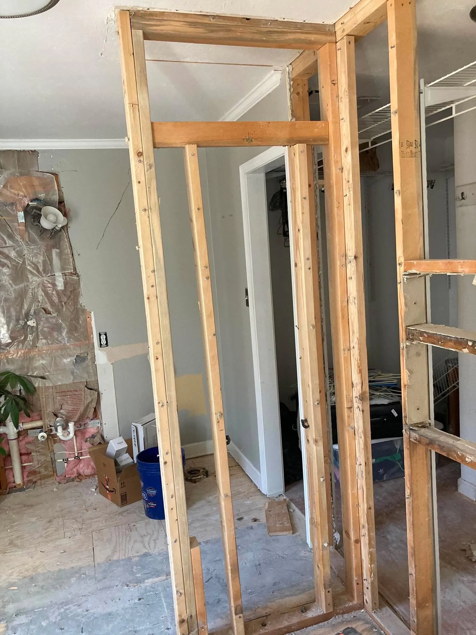 Exposed wood stud framing around a doorway opening into a closet with wire shelving visible beyond.