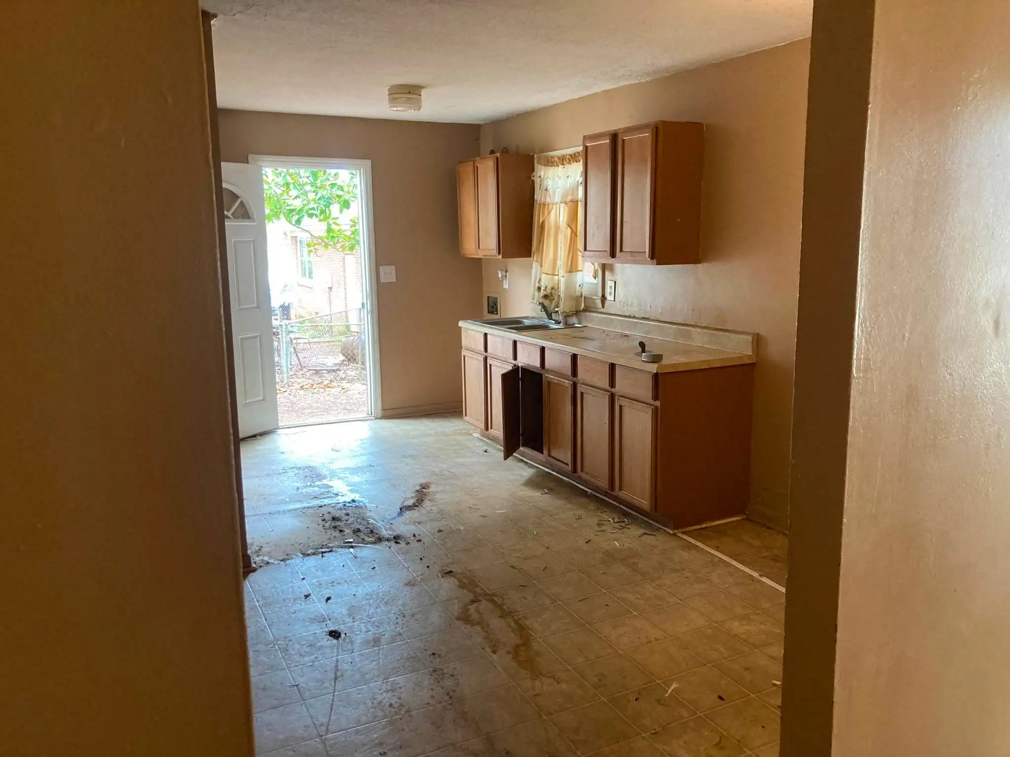 An emptied kitchen with the cabinets still in place and daylight coming through the open back door